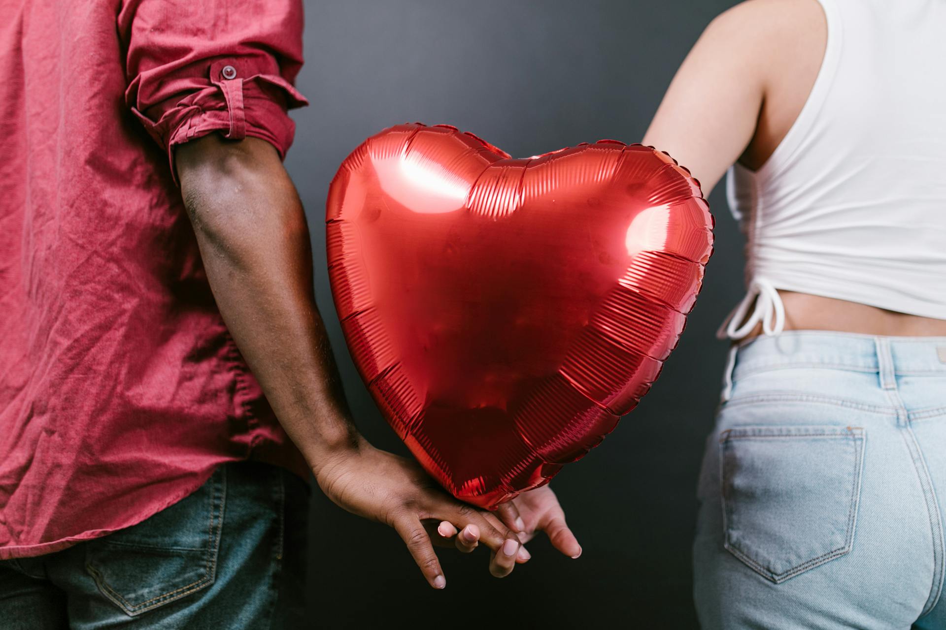 couple holding a red heart shaped balloon between them