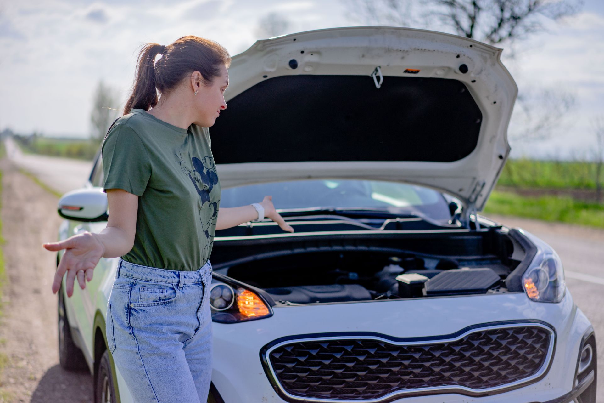 a confused woman stands by a car with an open hood