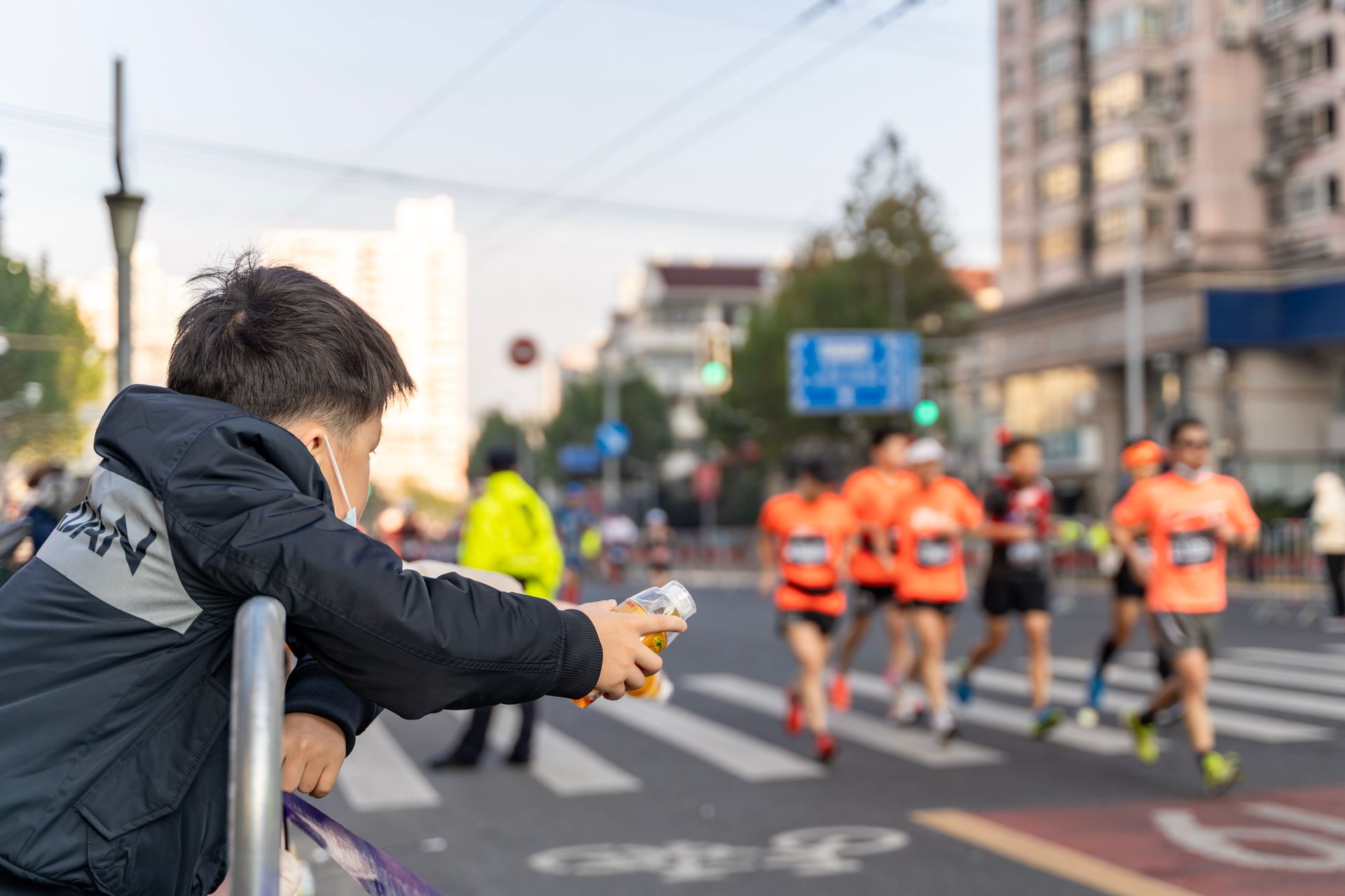 a child leans on the barrier watching marathon runners