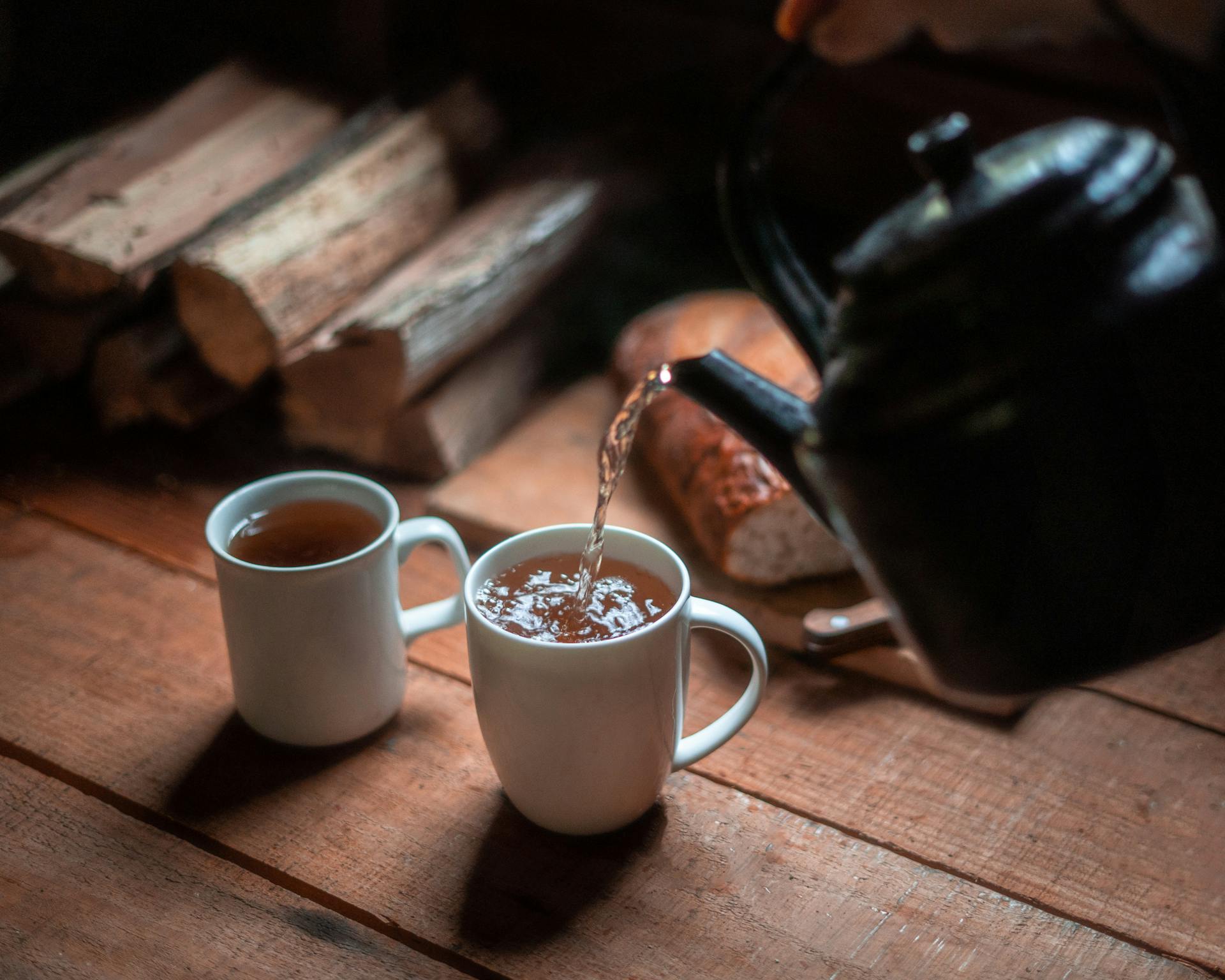 a kettle pouring hot water into two mugs of tea