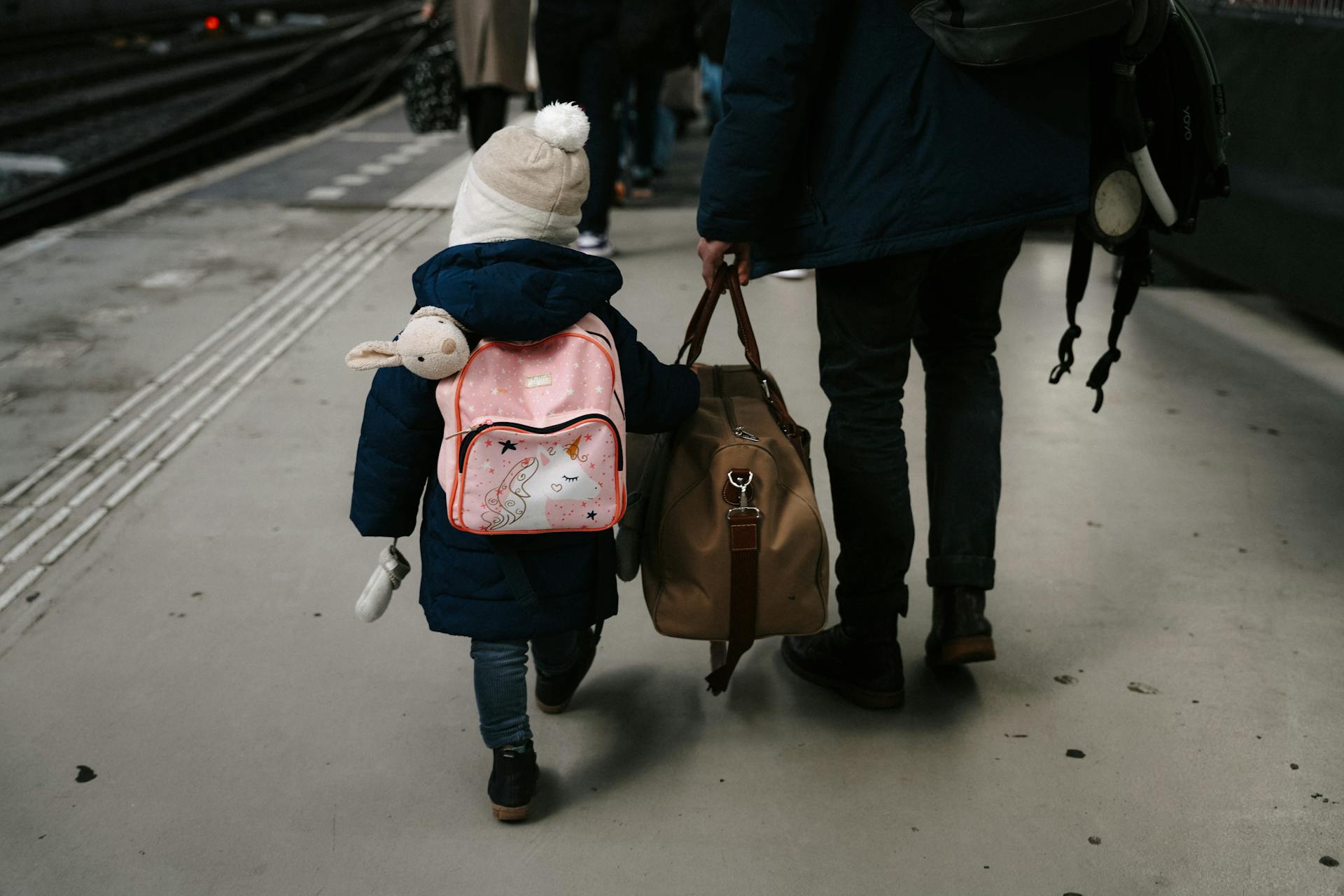 child traveling with adult standing on train platform