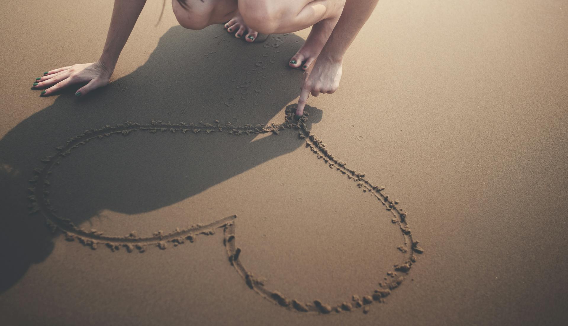 person draws heart in the sand
