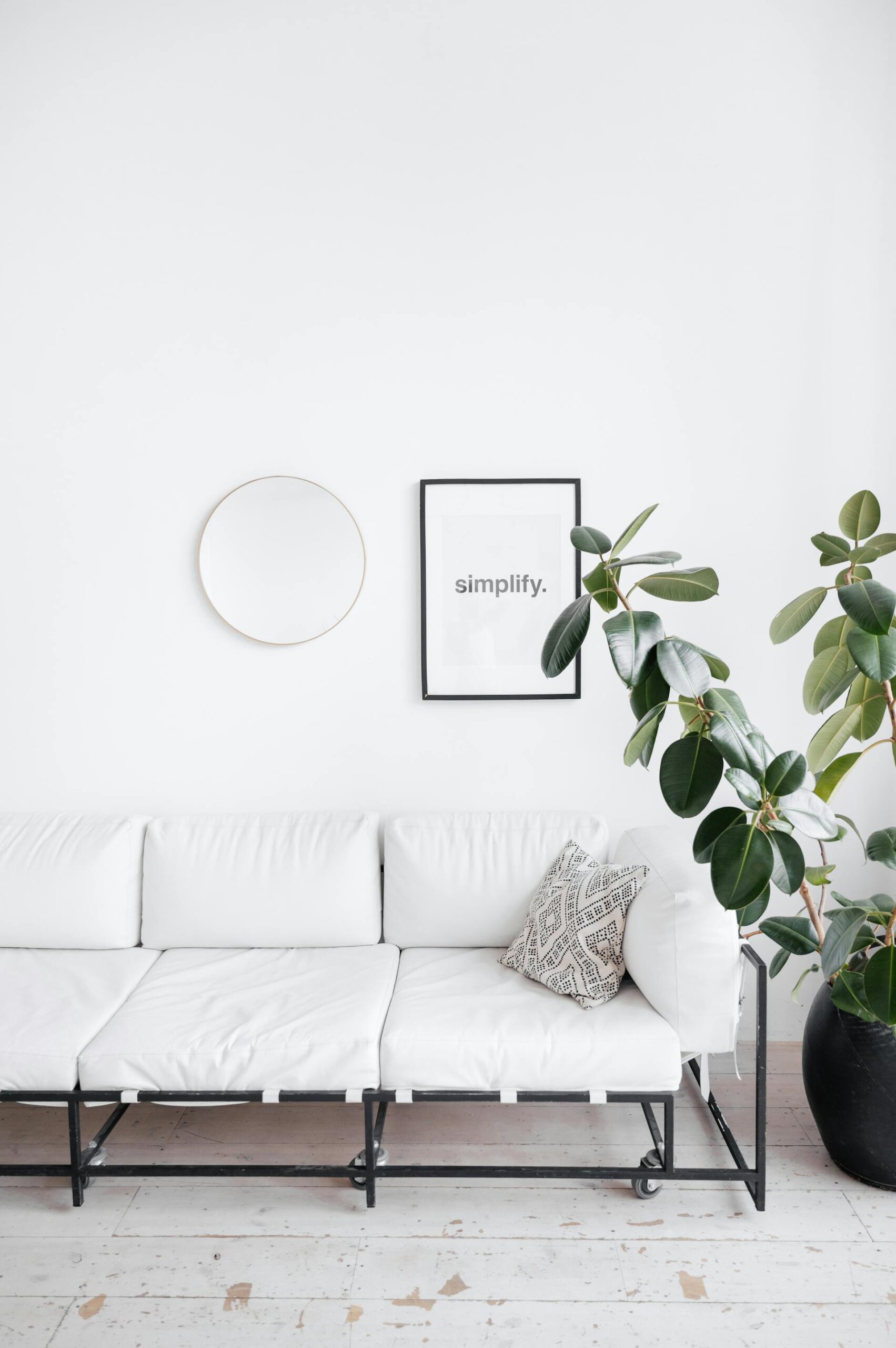 a white sofa besdie a potted tree with a sign that reads simplify